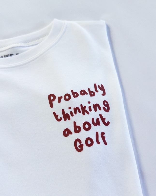 White t-shirt with red text 'Probably thinking about Golf' on a light gray background