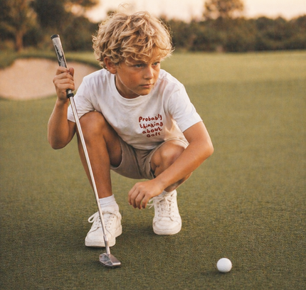 Young boy on a golf course preparing to putt with a golf club and ball.