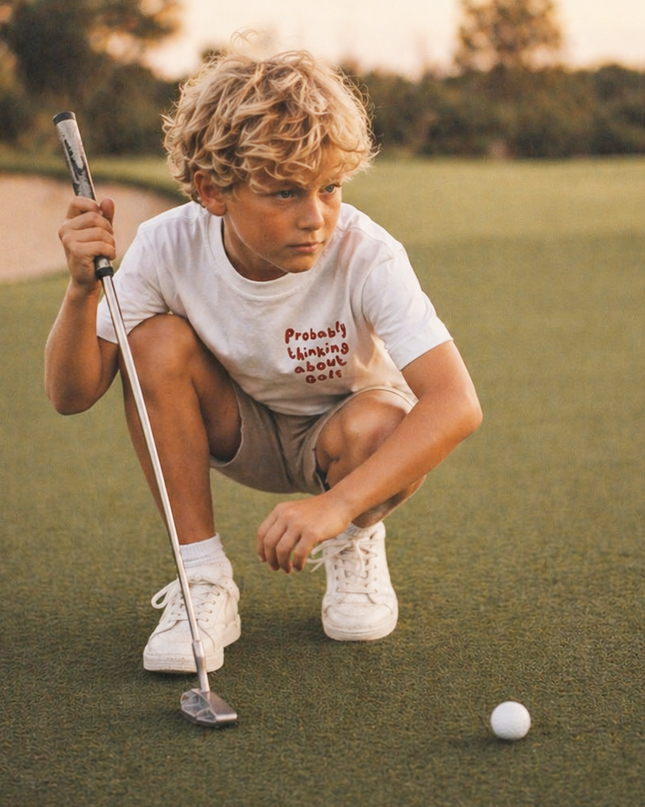 Young boy on a golf course preparing to putt with a golf club and ball.