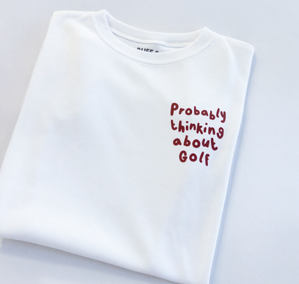 White t-shirt with red text 'Probably thinking about Golf' on a light gray background