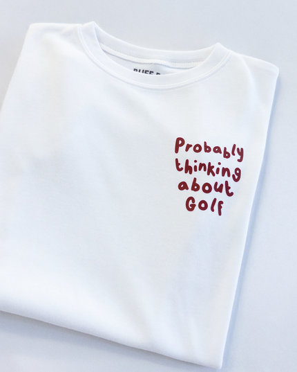 White t-shirt with red text 'Probably thinking about Golf' on a light gray background