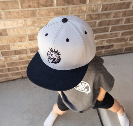 Child wearing a cap and gray shirt against a brick wall