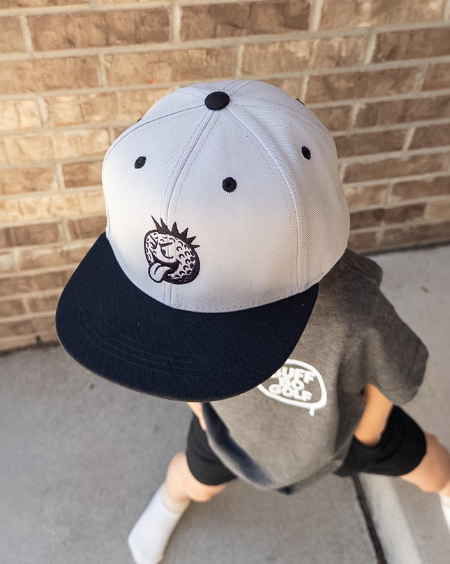 Child wearing a cap and gray shirt against a brick wall