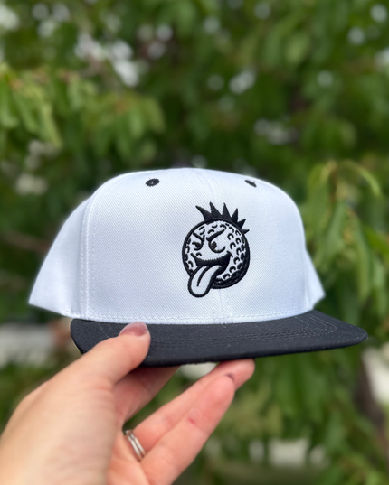 White cap with black logo held by a hand against a blurred green background