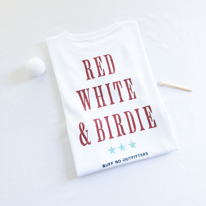 Folded white t-shirt with bold red text reading “RED WHITE & BIRDIE” and three light blue stars underneath, branded with “BUFF BO OUTFITTERS” at the bottom; styled with a white golf ball and wooden tee on a white background.
