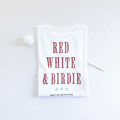 Folded white t-shirt with bold red text reading “RED WHITE & BIRDIE” and three light blue stars underneath, branded with “BUFF BO OUTFITTERS” at the bottom; styled with a white golf ball and wooden tee on a white background.

