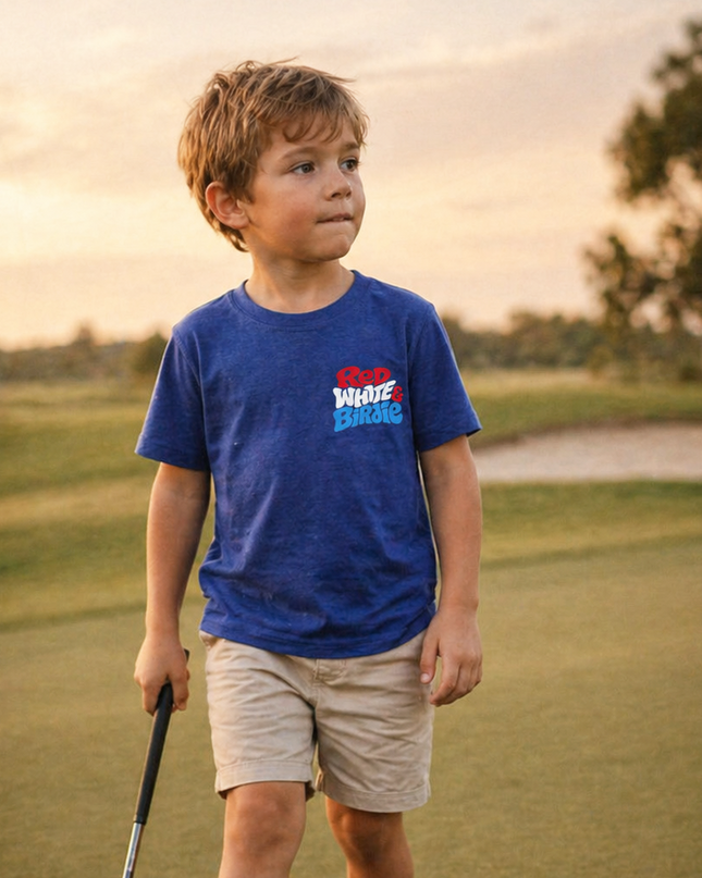 Young boy on a golf course holding a club and ball, wearing a blue t-shirt with a logo.