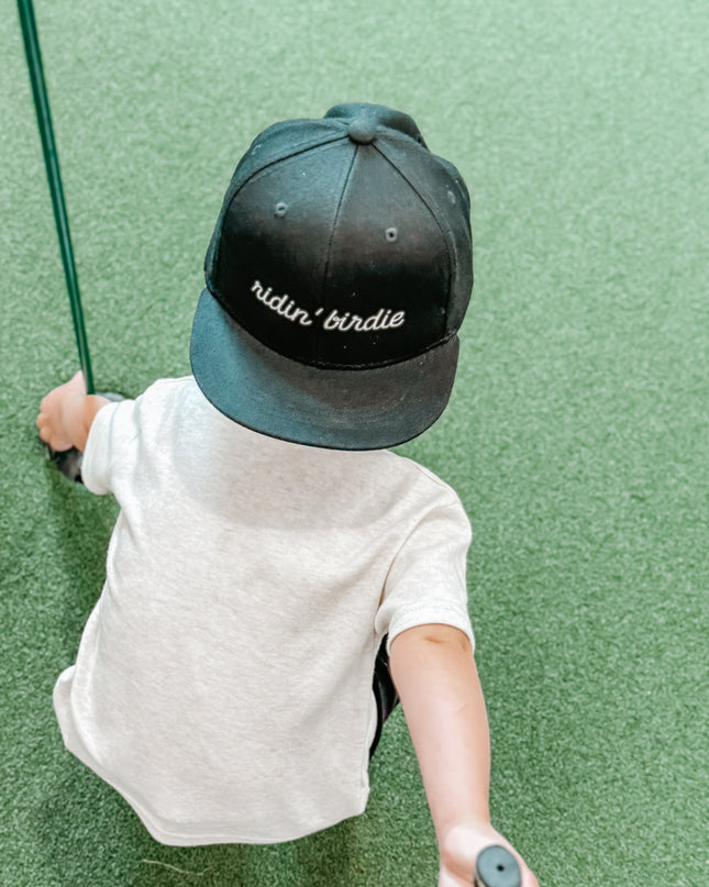 Child wearing a cap with 'ridin' birdie' on a green golf course