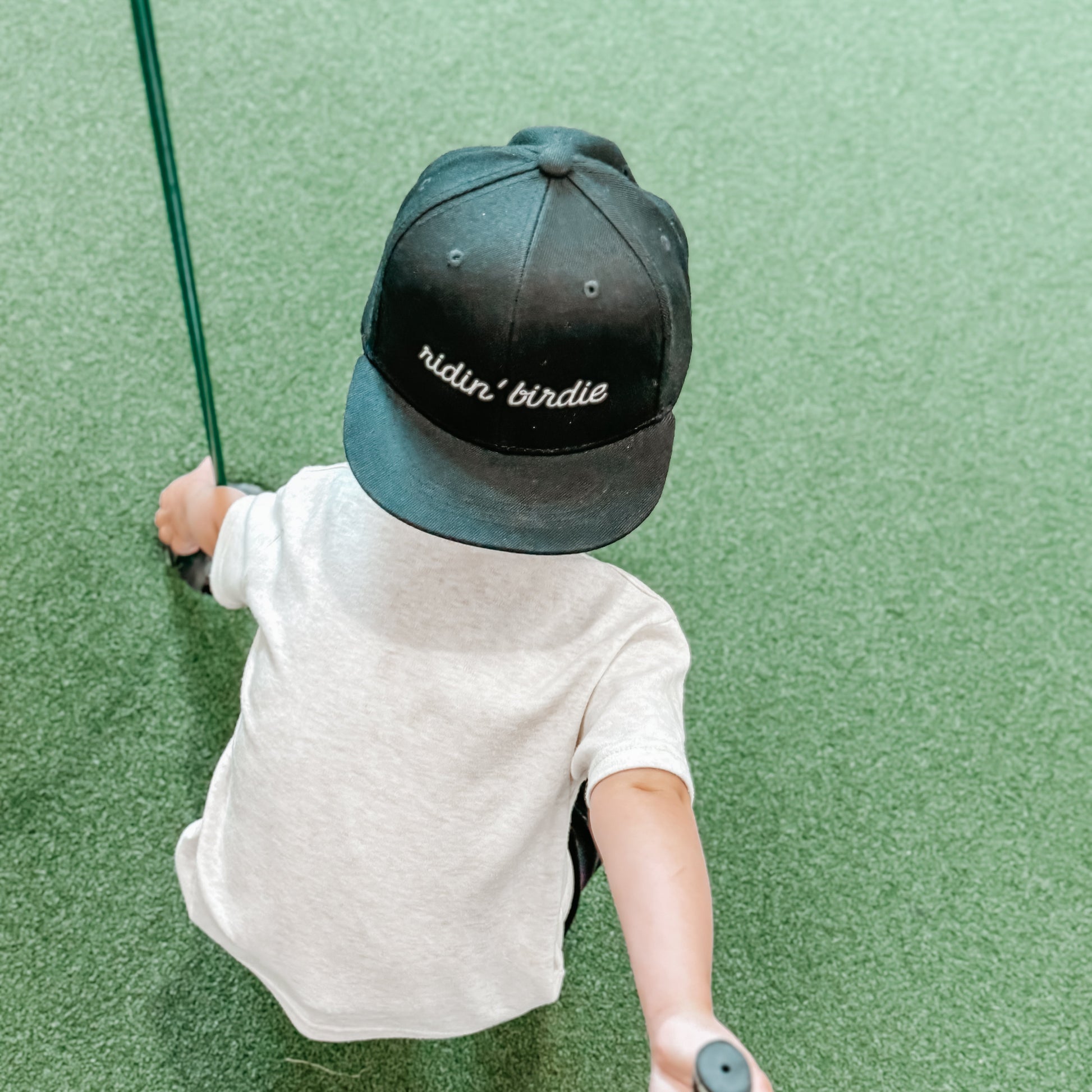 Child wearing a cap with 'ridin' birdie' on a green golf course