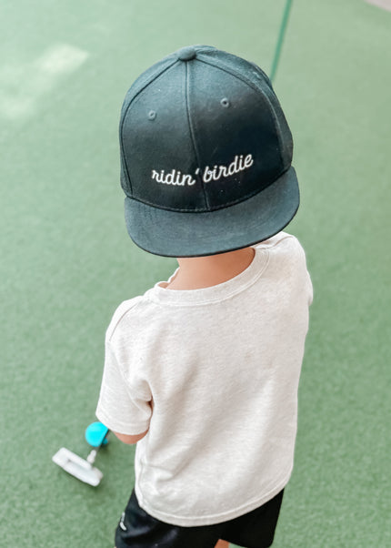 Child wearing a cap with text, standing on a green surface