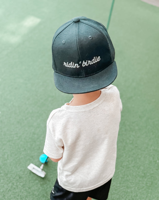 Child wearing a cap with text, standing on a green surface