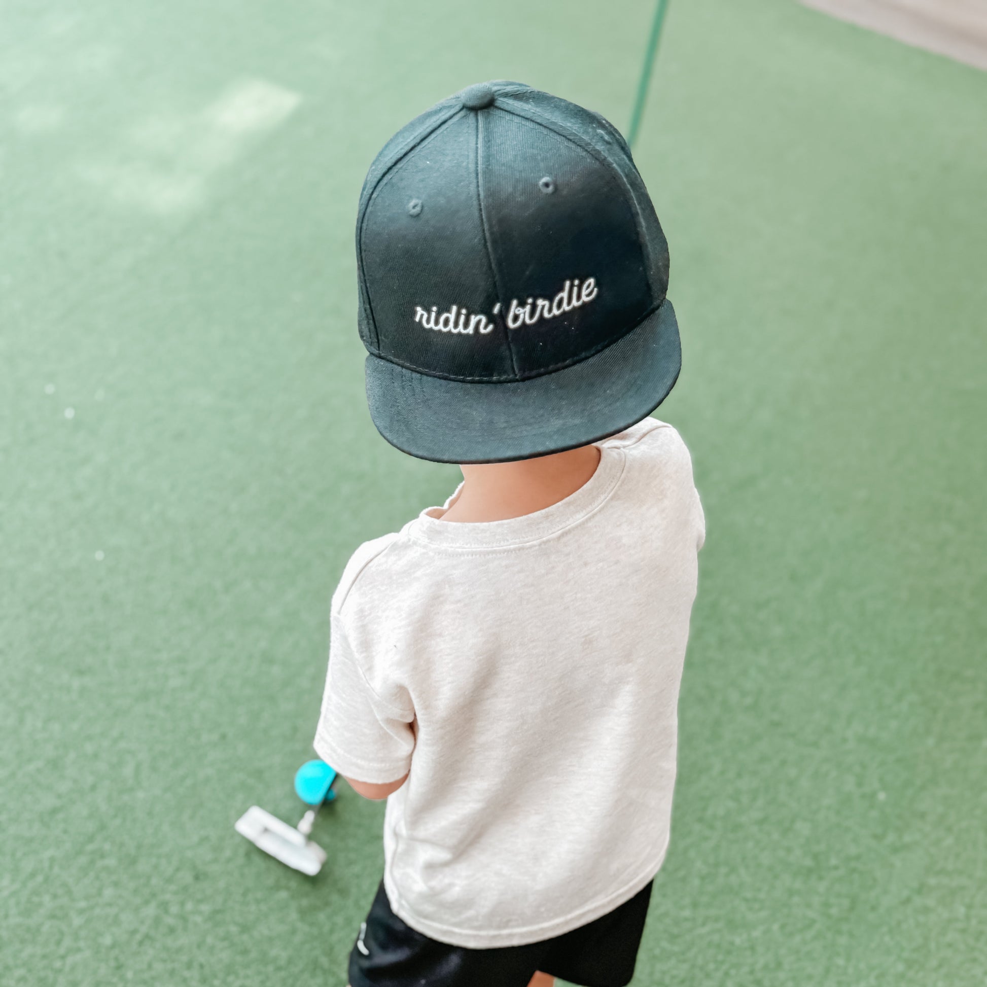 Child wearing a cap with text, standing on a green surface