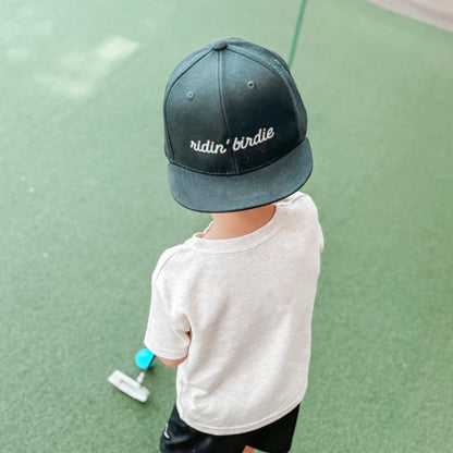 Child wearing a cap with text, standing on a green surface