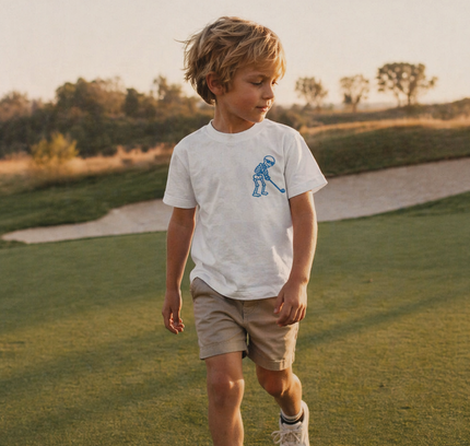 Child walking on a golf course wearing a white t-shirt with a logo.