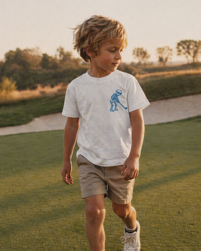Child walking on a golf course wearing a white t-shirt with a logo.