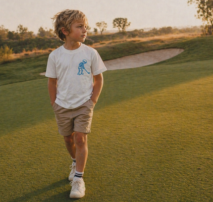 Young boy walking on a golf course with trees and a path in the background