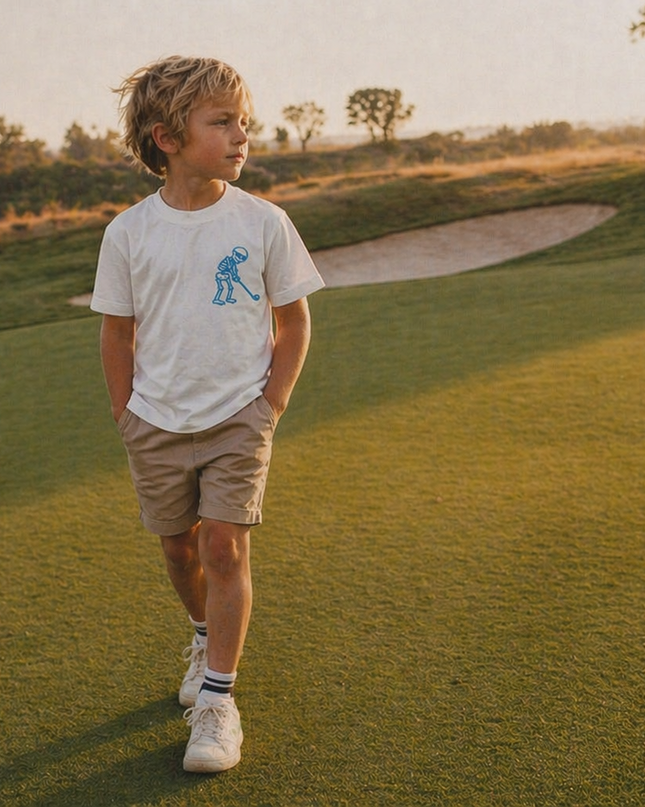 Young boy walking on a golf course with trees and a path in the background