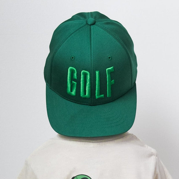 Person wearing a green 'GOLF' cap and a white t-shirt with a skeleton design on a plain background