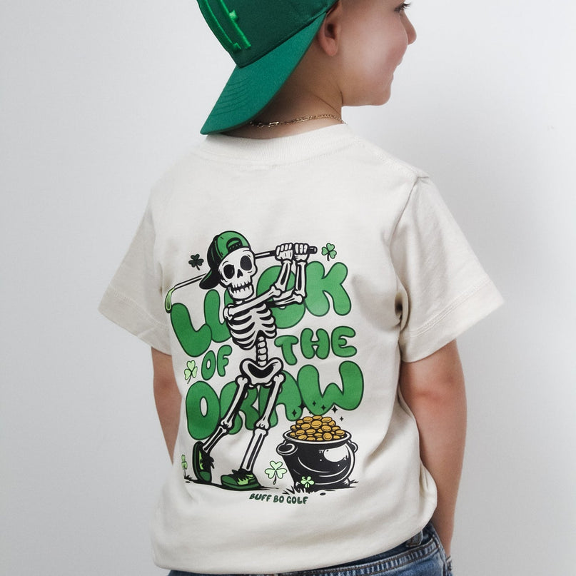 Child wearing a white t-shirt with a graphic design and a green cap on a plain background