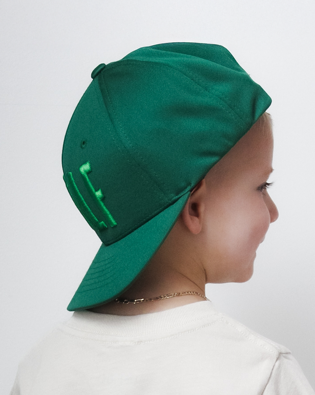 Child wearing a white t-shirt with a graphic design and a green cap on a plain background