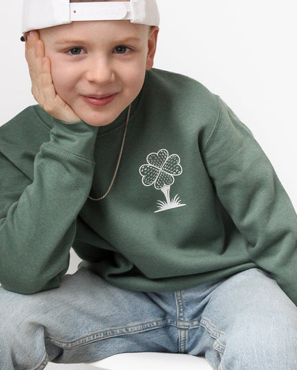 Child wearing a green sweatshirt with a white logo and a white cap, sitting on a white chair against a light gray background.