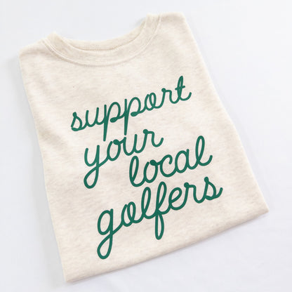 Buff Bo Outfitters' 'Support Your Local Golfers' kids' t-shirt in soft cream. A stylish and comfortable tee celebrating young golfers and the love of the game.