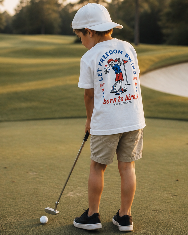 Child on a golf course wearing a white t-shirt with graphics and text.