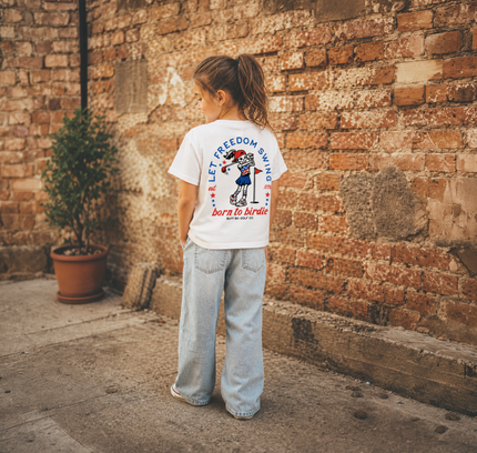 Child wearing a white t-shirt with text and graphics, standing against a brick wall.