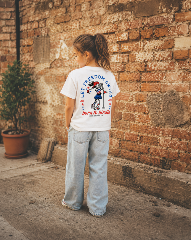 Child wearing a white t-shirt with text and graphics, standing against a brick wall.