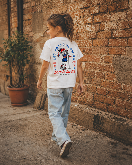 Child walking on a street wearing a t-shirt with text and graphics.