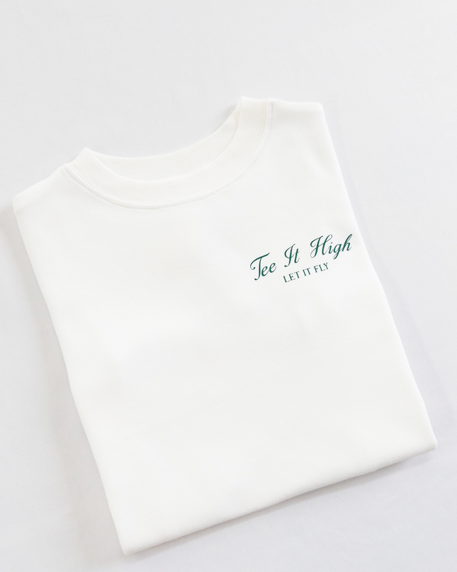 White kids golf t-shirt with minimalist green text on the chest reading 'Tee It High, Let It Fly,' folded neatly on a light background, perfect for young golfers and golf fans.