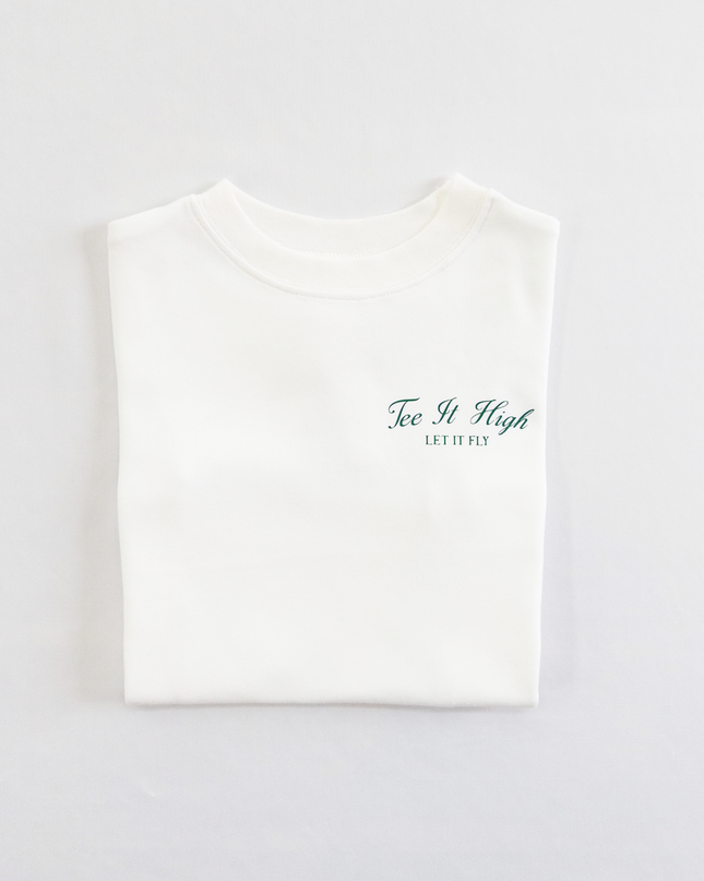 White kids golf t-shirt with minimalist green text on the chest reading 'Tee It High, Let It Fly,' folded neatly on a light background, perfect for young golfers and golf fans.