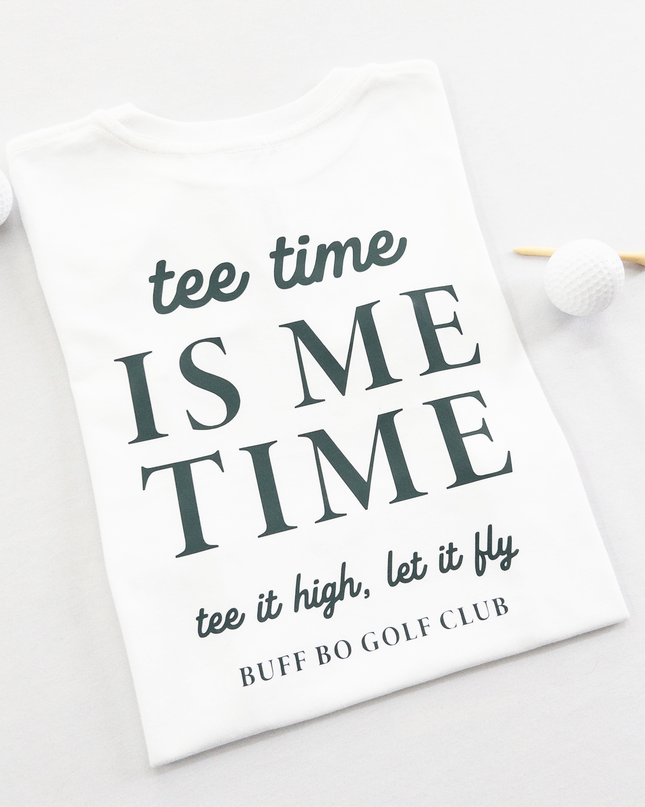 White kids golf t-shirt featuring dark green text reading 'tee time is me time' with additional script text 'tee it high, let it fly' and 'Buff Bo Golf Club,' styled flat with golf balls and a wooden tee, fun and motivational golf apparel for kids.