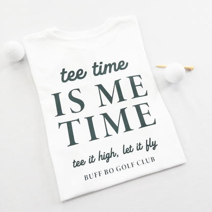 White kids golf t-shirt featuring dark green text reading 'tee time is me time' with additional script text 'tee it high, let it fly' and 'Buff Bo Golf Club,' styled flat with golf balls and a wooden tee, fun and motivational golf apparel for kids.