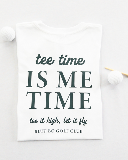 White kids golf t-shirt featuring dark green text reading 'tee time is me time' with additional script text 'tee it high, let it fly' and 'Buff Bo Golf Club,' styled flat with golf balls and a wooden tee, fun and motivational golf apparel for kids.
