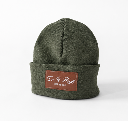 An olive green knit beanie hat with a brown leather patch on the front cuff that reads 'Tee It High LET IT PEI'.