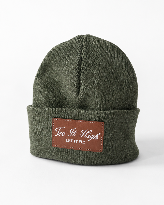 An olive green knit beanie hat with a brown leather patch on the front cuff that reads 'Tee It High LET IT PEI'.