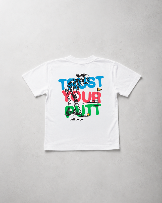 A white short-sleeve t-shirt laid flat on a light gray textured background, featuring a colorful graphic print on the back with the text 'TRUST YOUR BUTT' in blue, red, and green, and a cartoon character wearing sunglasses.