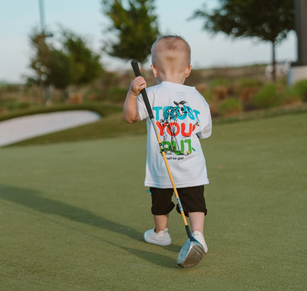 Child holding a golf club on a golf course with a humorous t-shirt