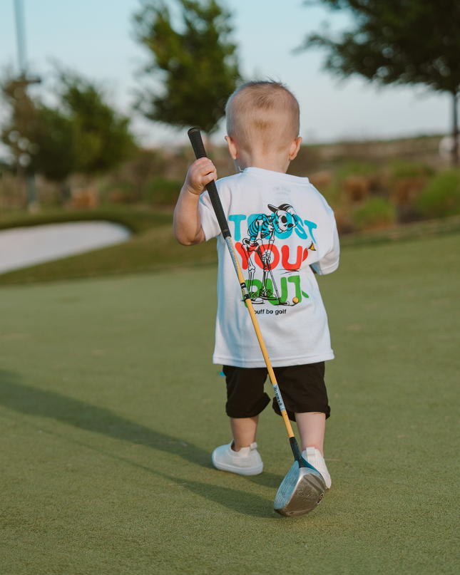 Child holding a golf club on a golf course with a humorous t-shirt