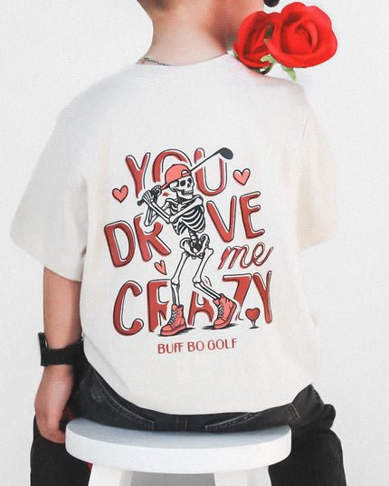 Child wearing a white t-shirt with skeleton design and text, sitting on a stool with red roses.
