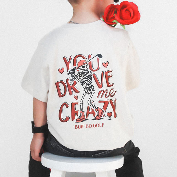 Child wearing a white t-shirt with skeleton design and text, sitting on a stool with red roses.